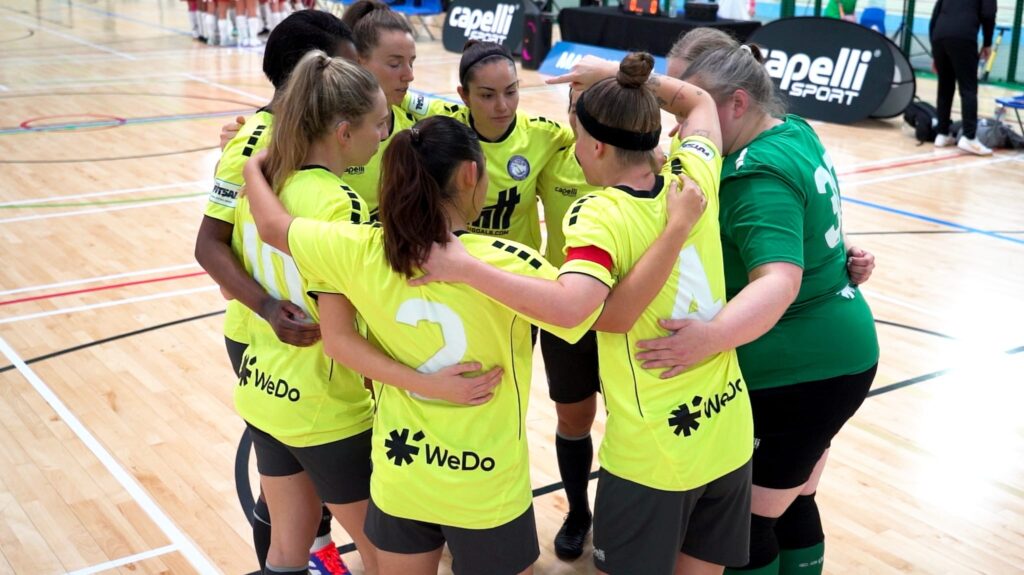 Women’s futsal team in a pre-match huddle on an indoor court,