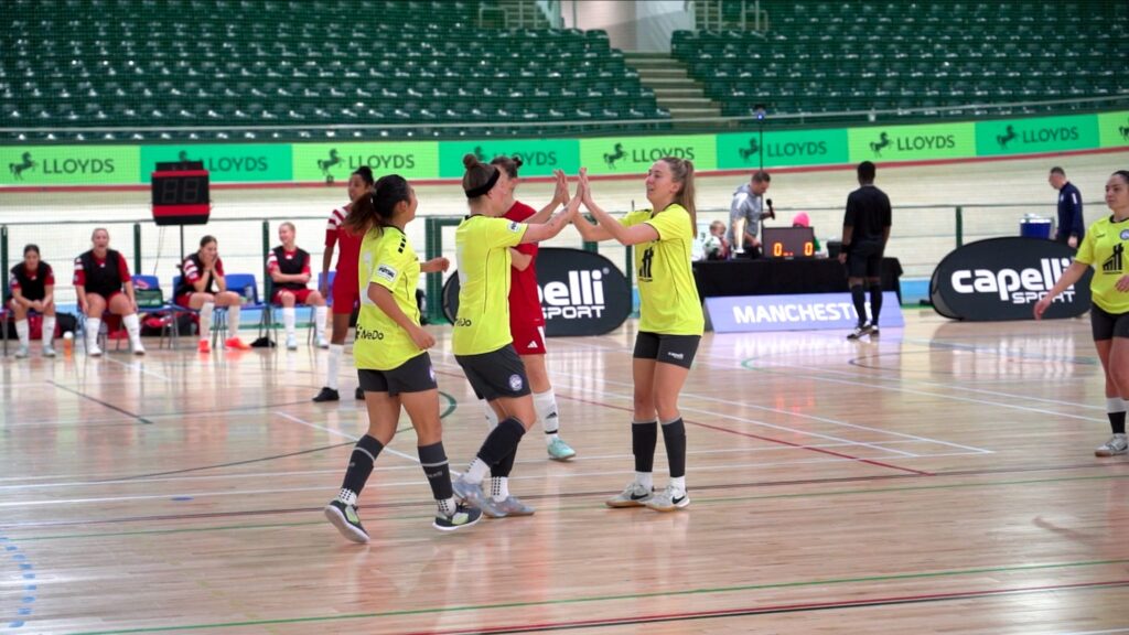 Women futsal teammates celebrating with a high-five during an indoor league match.